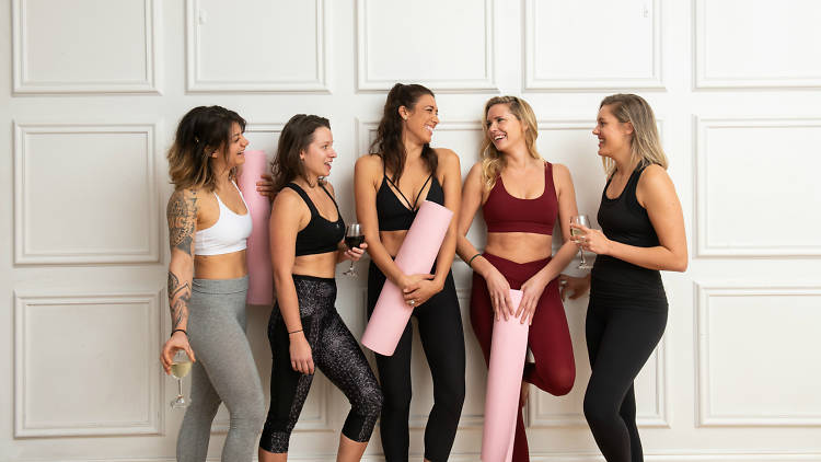 Five women wearing yoga clothes and holding glasses of wine
