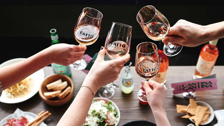 Found hands holding out four glasses of rosé over a table of food