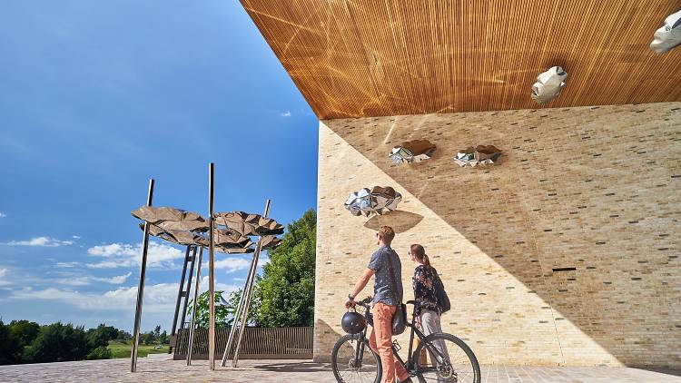 Two people looking up at artwork installation of chrome clouds, one is walking a bike