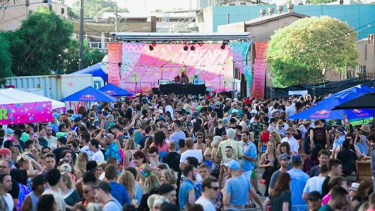 A festival crowd assembled in front of a stag with a large pink back-drop emblazoned with the 'Heaps Gay' logo