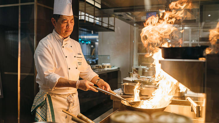 A chef frying noodles in a flaming wok