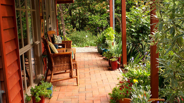 Two wicker chairs on a brick verandah surrounded by plants