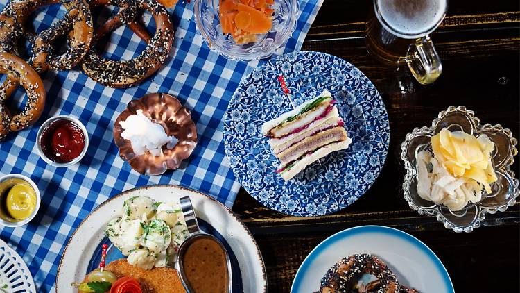 A gingham covered table topped with pretzels, beers, schnitzels and sandwiches