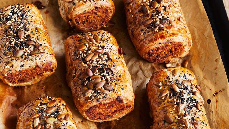A tray of freshly baked sausage rolls covered in seeds