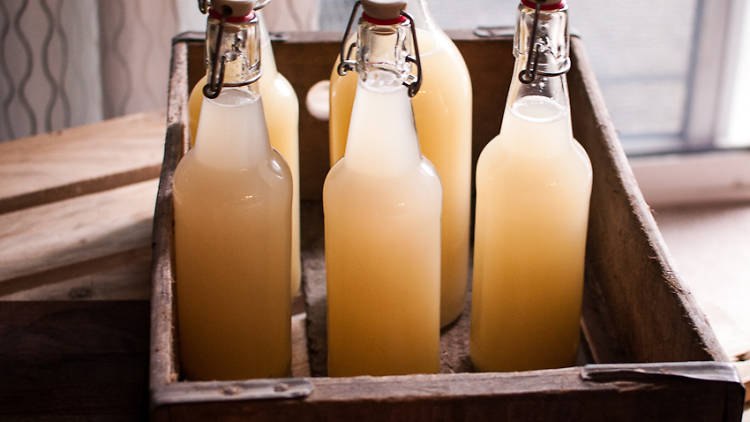 Glass bottles of traditional cloudy ginger beer sit in a wooden box.