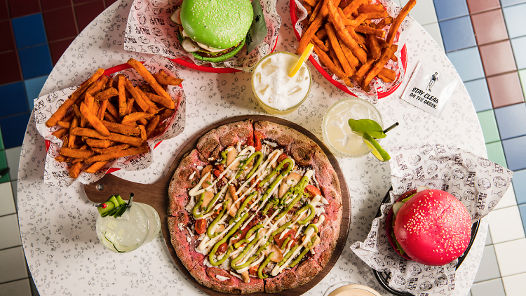 A birds-eye view of a table of food including pizza, bowls of sweet potato fries and two burgers. 