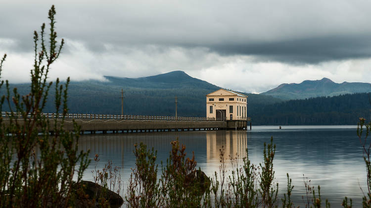 A house at the end of a long pier on a lake surrounded by mountains