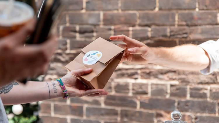 A person with wrist tattoos accepts a gift bag with a Something for Jess sticker on it.