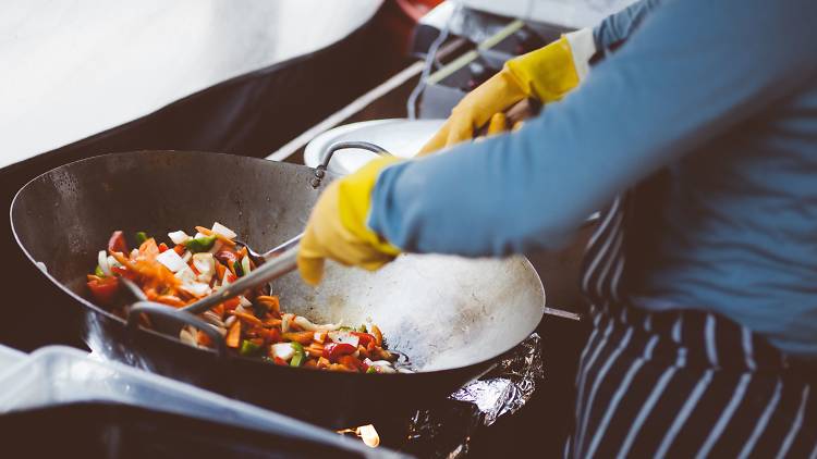 Chef with tongs tosses food in a wok