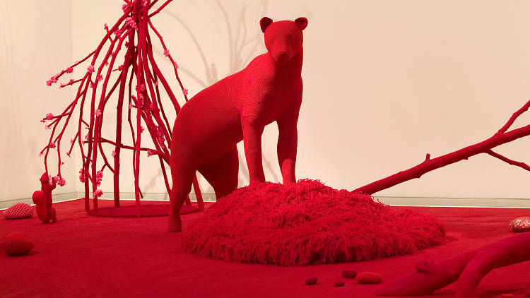 An installation of a red crocheted bear standing on a matching red crocheted landscape
