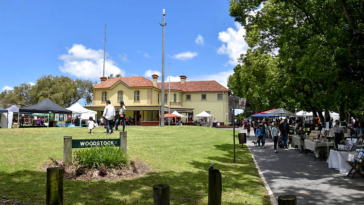 A large old style building sits amongst green lawns, market stalls are off to the right.