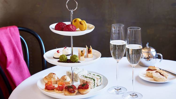 Three tiers of high tea snacks on a table with two glasses of Champagne