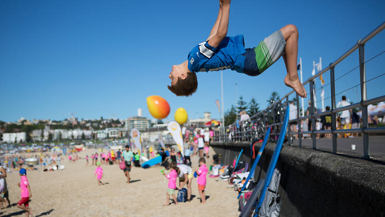 Boy doing backflip off a wall onto the beach.