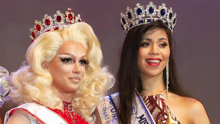 A drag queen and a beauty queen pose with crowns.