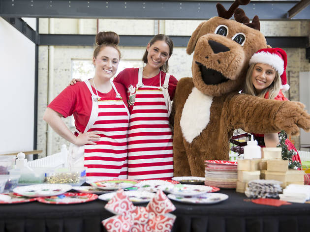 The Cannery Christmas Three people in striped red aprons pose with a giant reindeer.