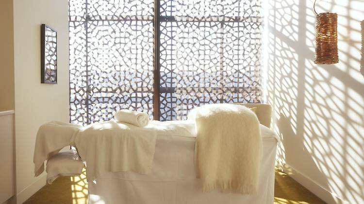 A  massage bed with white bedding and towels in front of a brightly lit window.