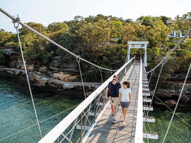 Bondi to Manly Coastal Walk Two people walk across a suspension bridge over water.