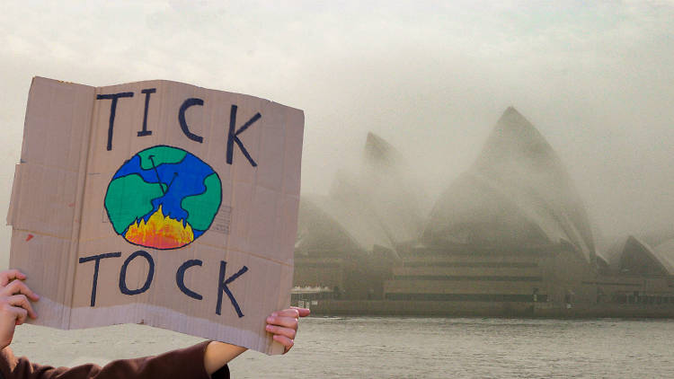 A person holds up a sign in front of the Sydney Opera House, which is blanketed in smoke, reading 'Tick Tock' with a painting of the earth in flames.