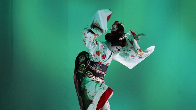 A performer in traditional Kabuki costume dances in front of a turquoise background.