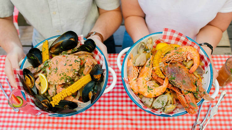 Two people holding plates of seafood, including prawns, mussels and whole crab