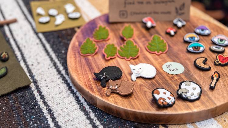 A collection of fabric patches sit on a wooden board, there are sleeping cats, eyes, and leaves. 