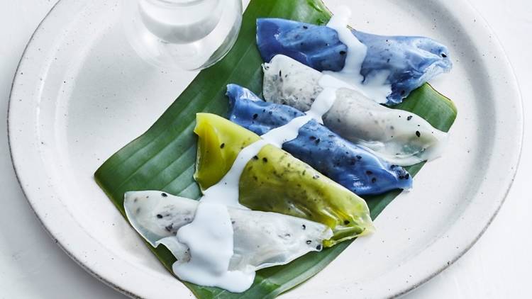 A plate of white, green and blue dessert dumplings on a banana leaf.