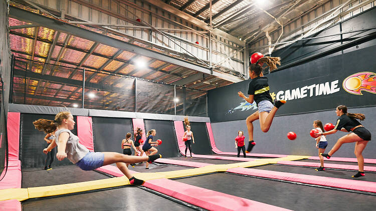 Teenagers bouncing on interconnected trampolines, one is bouncing up and throwing a foam ball