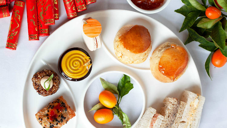 A white plate with lots of small pastries, scones and ribbon sandwiches on it
