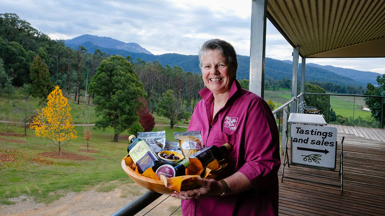 A woman with short hair holding a platter of olive oils and olives on a verandah