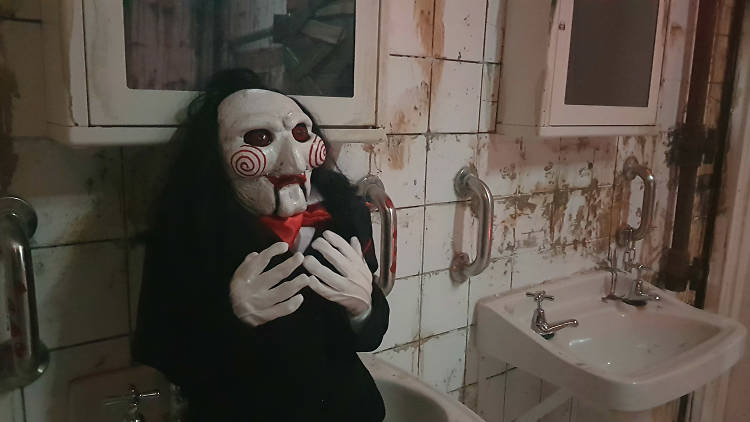 A Jigsaw Killer doll replica from the Saw movie franchise, sitting in a dingy bathroom