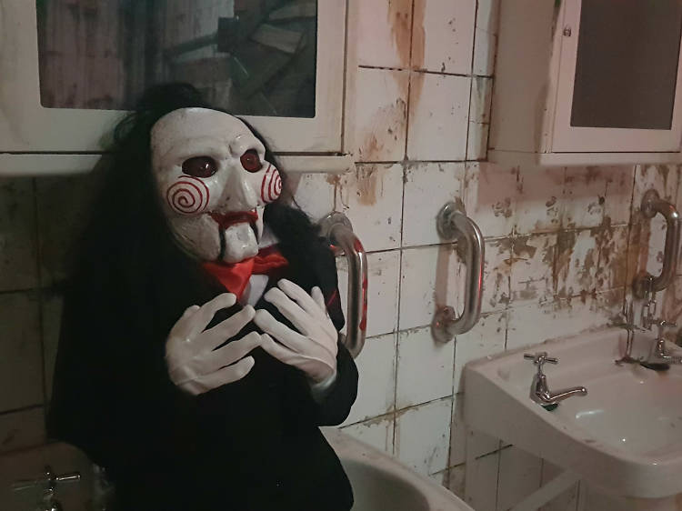 A Jigsaw Killer doll replica from the Saw movie franchise, sitting in a dingy bathroom