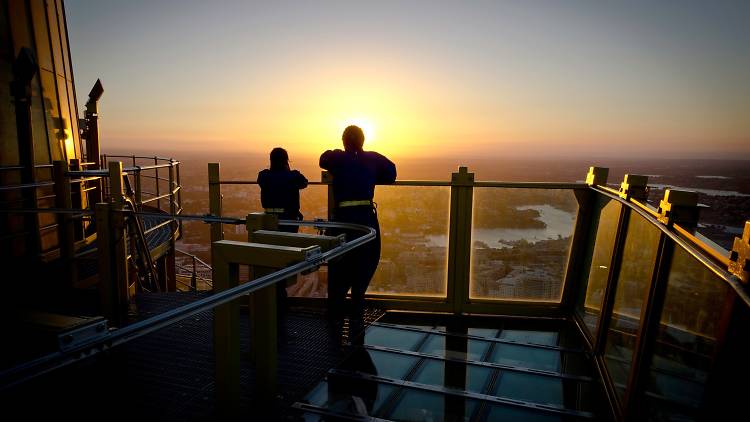 A couple is silhouetted against the sunset as they look out over the city from a great height. 