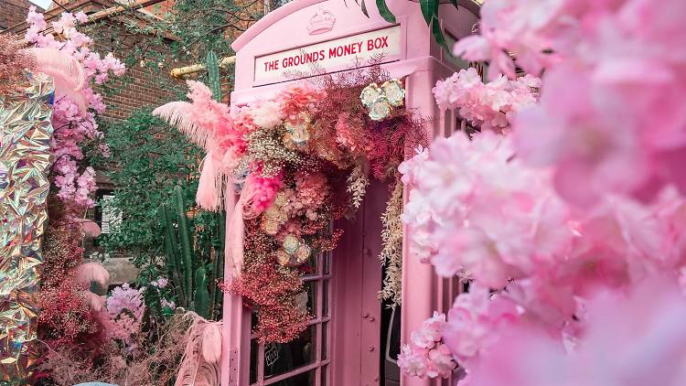 A pink phone booth amongst bunches of pastel flowers.