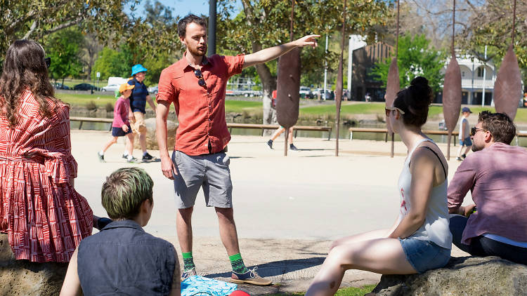 A man in a t-shirt and shorts talking to people at Birrarung Marr