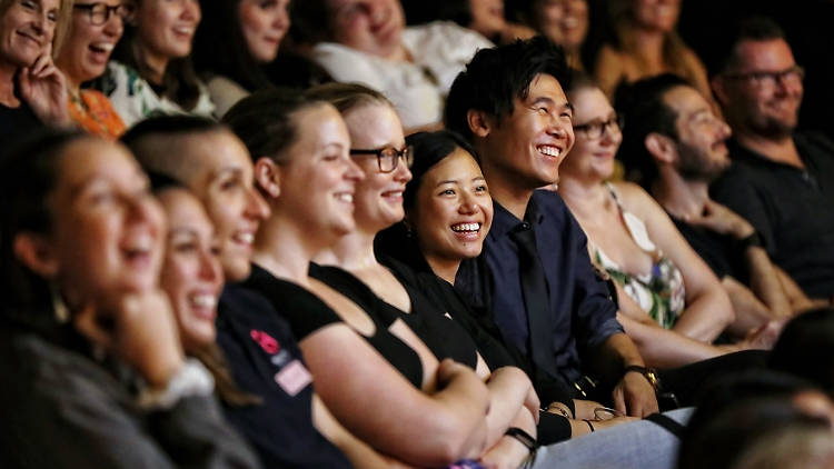 A diverse crowd of seated people are laughing.