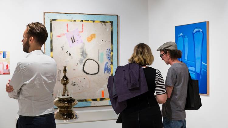 People peruse paintings in a gallery.