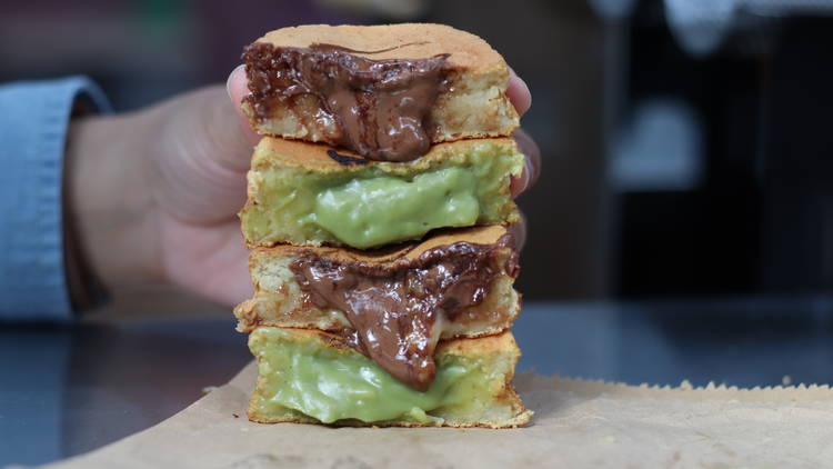 Two wheelcakes cut in half and stacked on top of each other as someone holds them up, with the custard oozing out of them