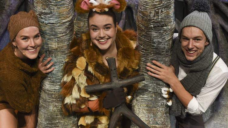 Three actors in animal-like costumes peeking out from behind trees on stage