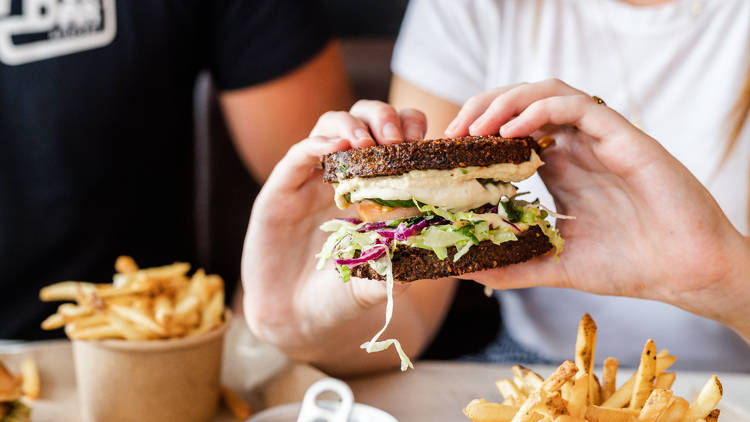 Two hands holding a burger with falafel buns