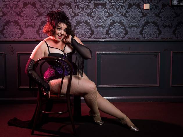Burlesque in Sydney A burlesque performer poses on a chair, she is wearing a corset, feathers and fringed gloves.