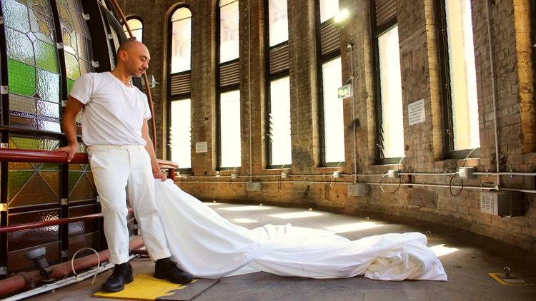 Man holding a white sheet in front of windows