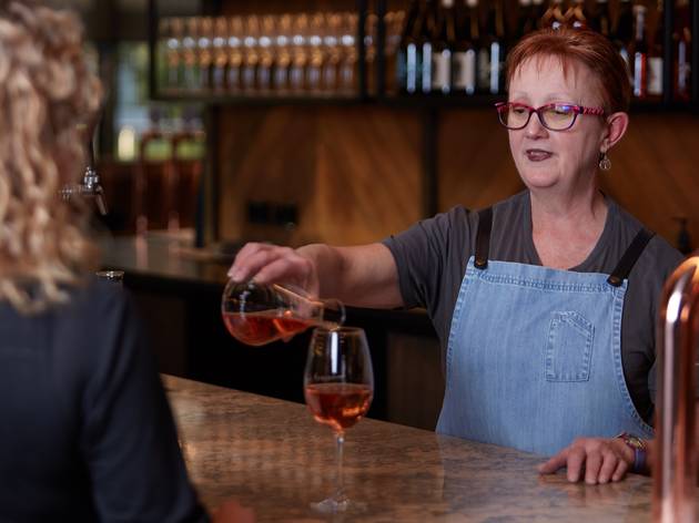 Innocent Bystander virtual wine tastings Woman wearing apron standing behind the bar pouring a glass of rose wine for a person