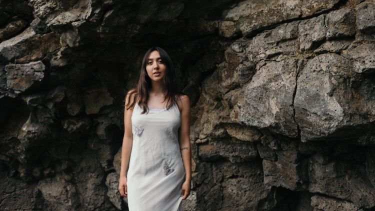 Alice Skye poses in a white dress in front of a rock face.
