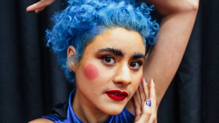 Montaigne poses with blue curly hair, red lipstick, red circles on her cheeks. 
