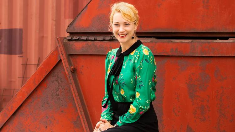 Writer Meg Mundell sitting against a red, industrial background