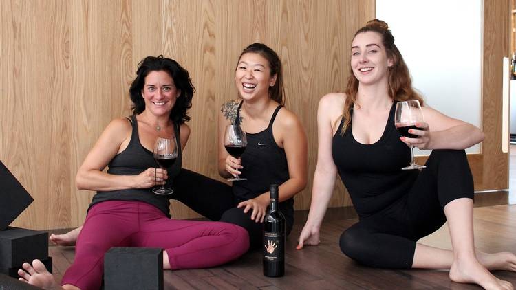 Three women in activewear sitting around drinking wine