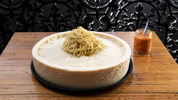 A wheel of pecorino cheese with fettuccine pasta inside on a table