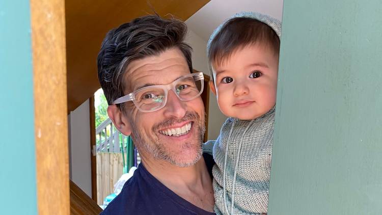 Osher opens the door, smiling, he is holding his infant son.