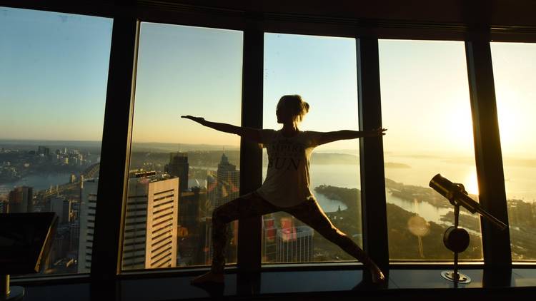 A yoga instructor holds a peaceful warrior pose, silhouetted against the Sydney skyline.