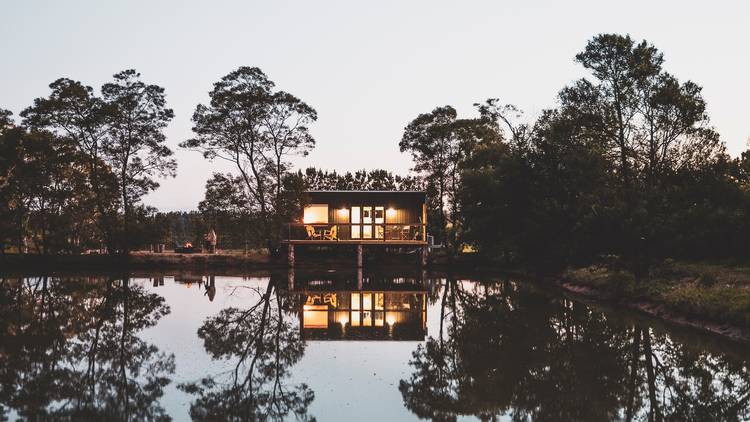 A tiny cabin sits in bushland on a dam.